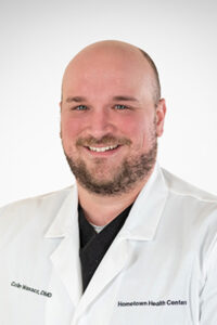A bald man in a white lab coat smiling.